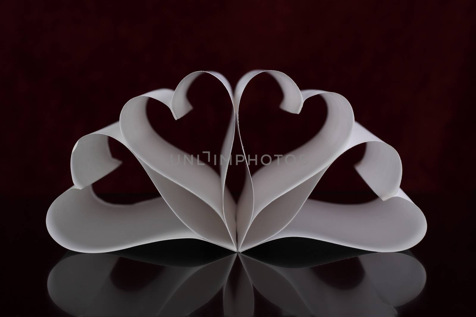 four paper hearts front view with red background and reflection on black table