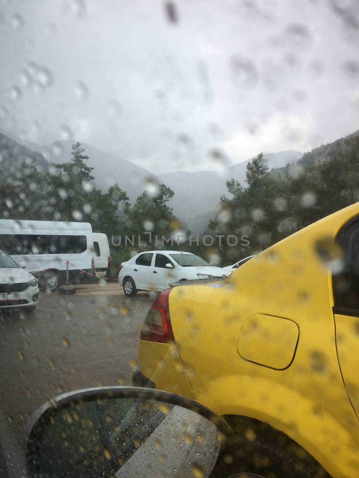 The road with the cars is photographed through the rain splattered windshield of the car.