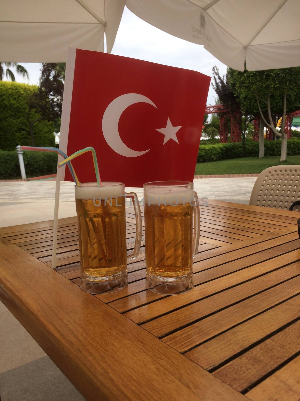 Two glasses of beer are on a wooden table in a Turkish hotel, near the flag of Turkey.