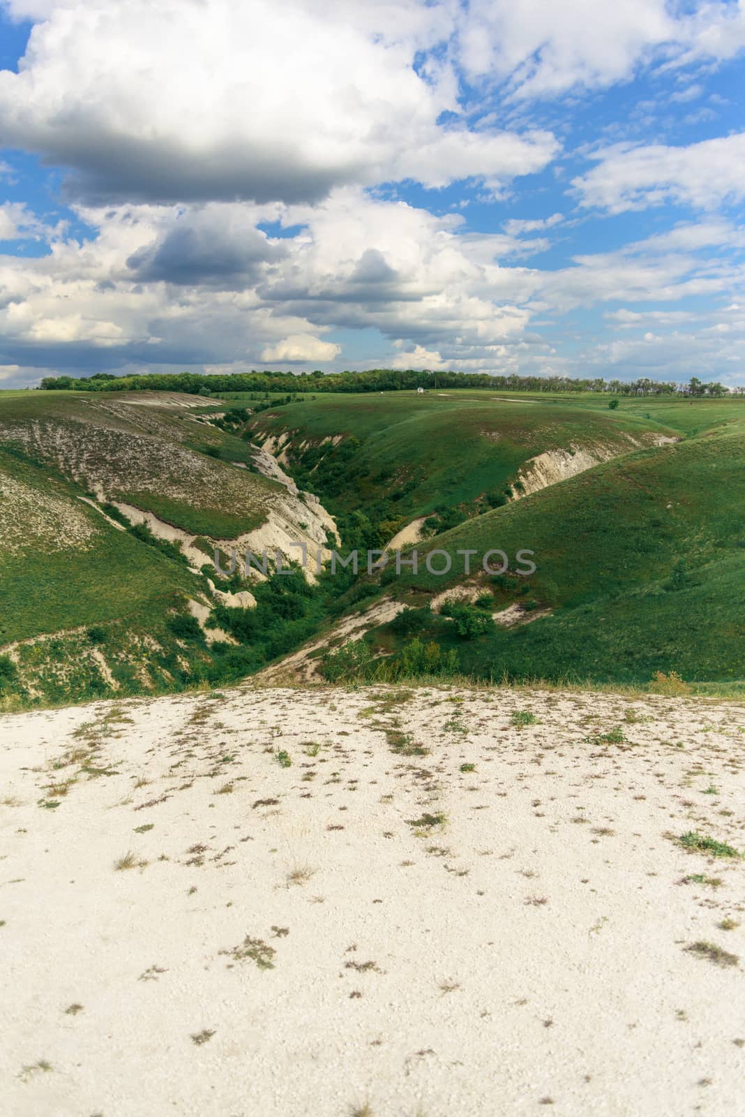 Beautiful view of grassy ravine on sky background with clouds, vertical shot.