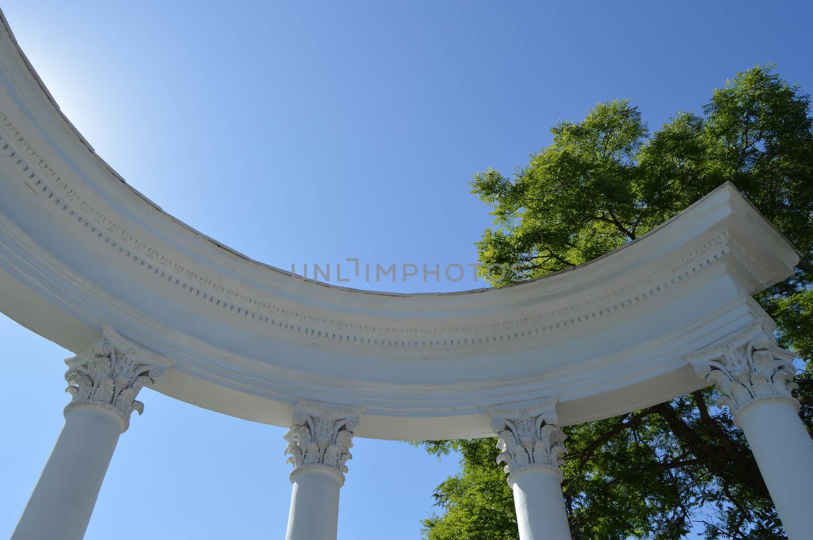 Part of a white rotunda with columns against a blue sky on a Sunny day.