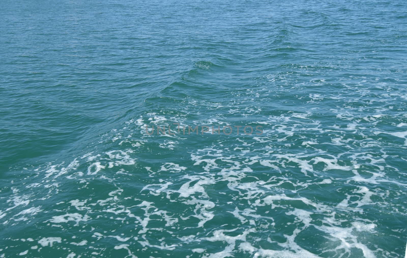 Background with wave and foam, trace on the surface of the water behind the fast moving ship.