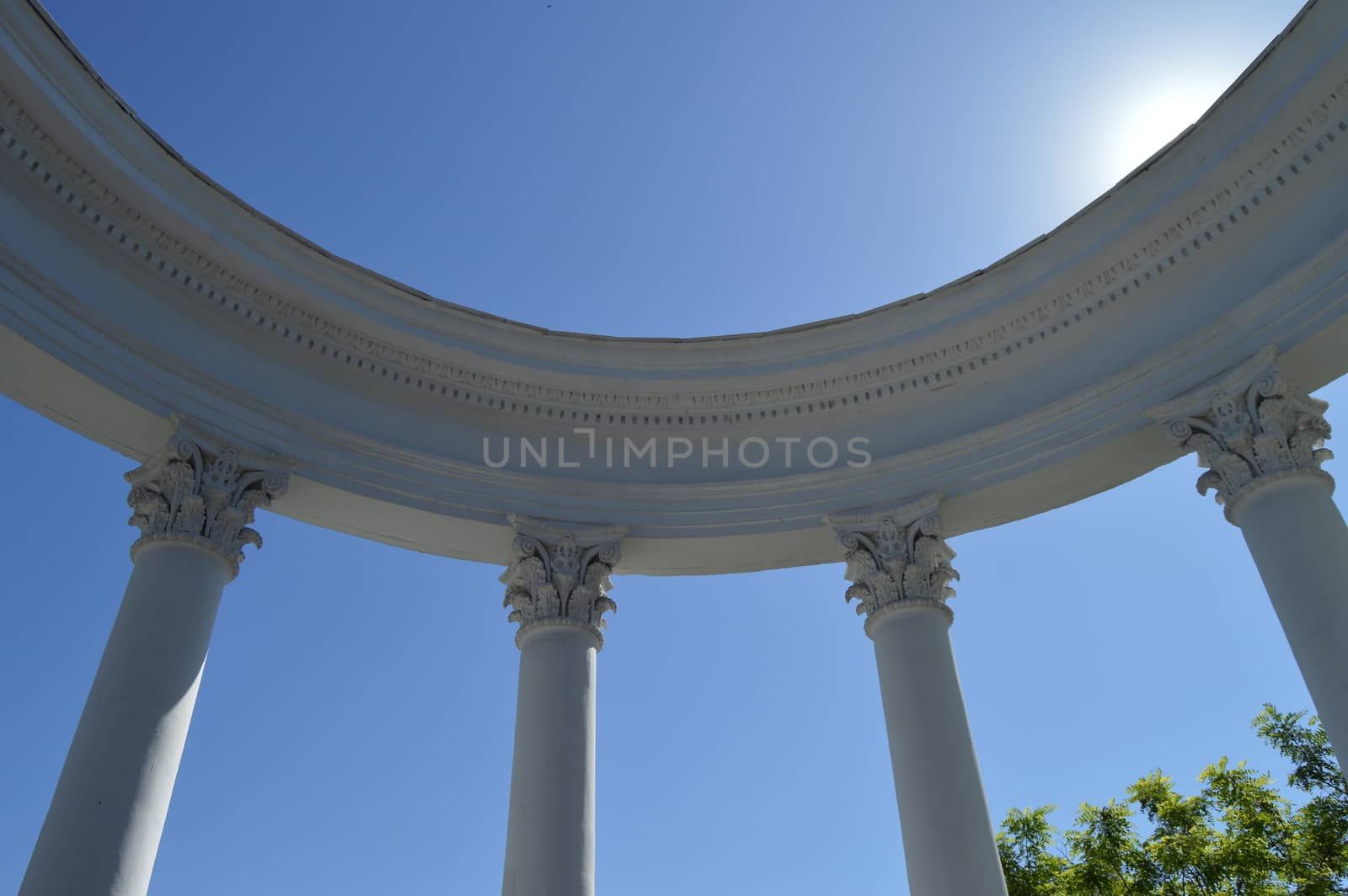 Part of a white rotunda with columns against a blue sky on a Sunny day.