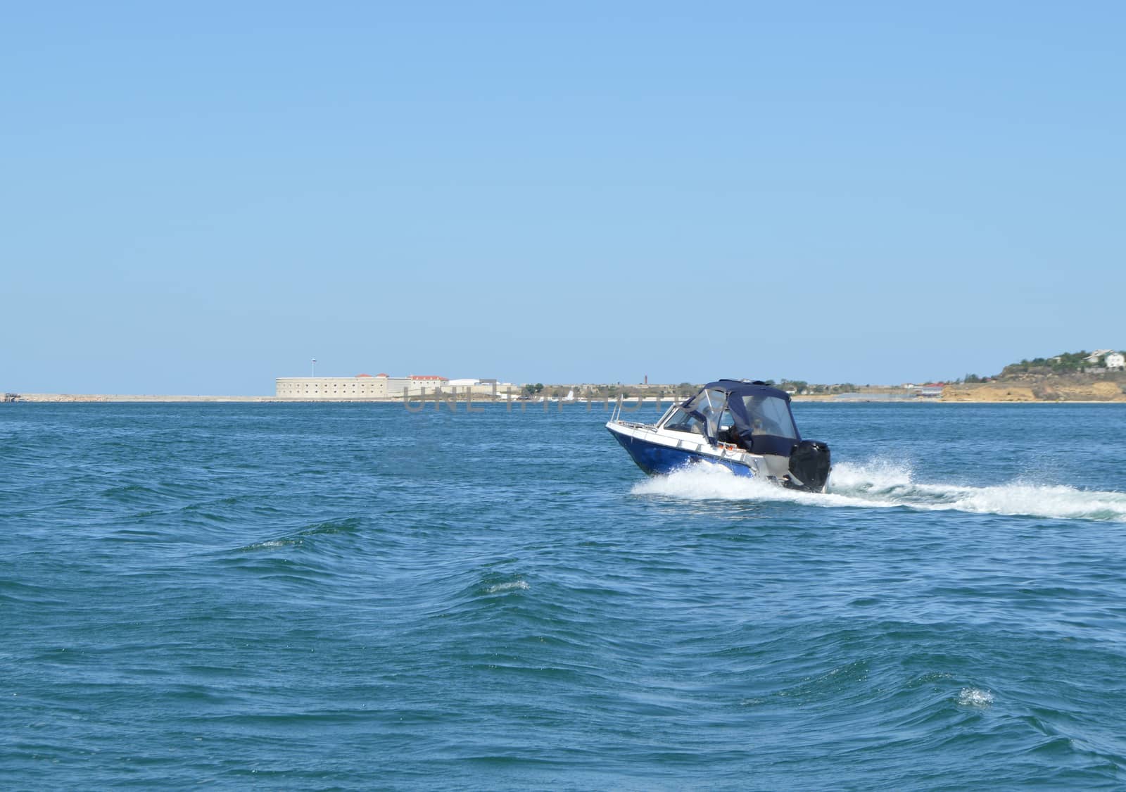 Motor boat moves along the sea along the shore, leaving a trail.