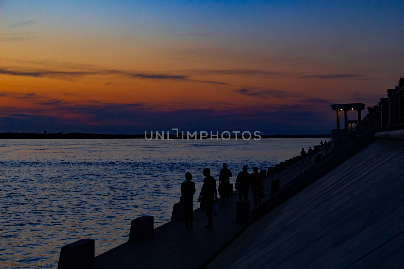 Sunset on the embankment of the Amur river in Khabarovsk. The sun set over the horizon. The embankment is lit by lanterns. People walk along the river Bank.
