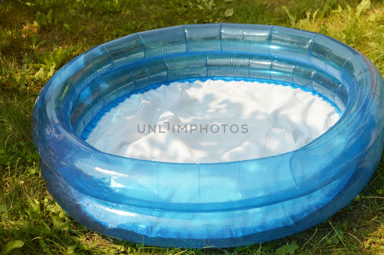 Round inflatable children's pool stands on the grass in the summer garden.