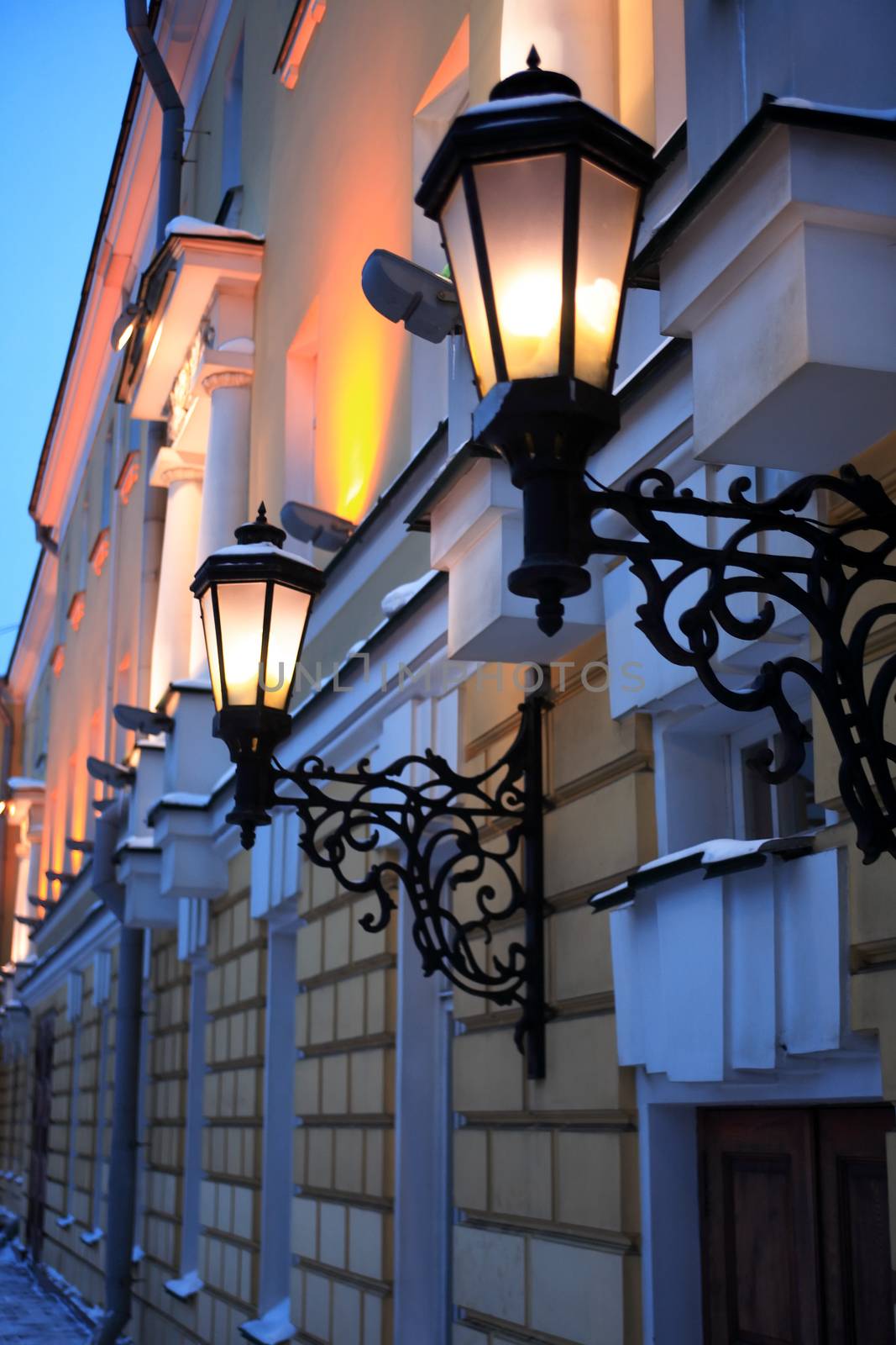 Nice old house wall with vintage iron glowing street lamp at night