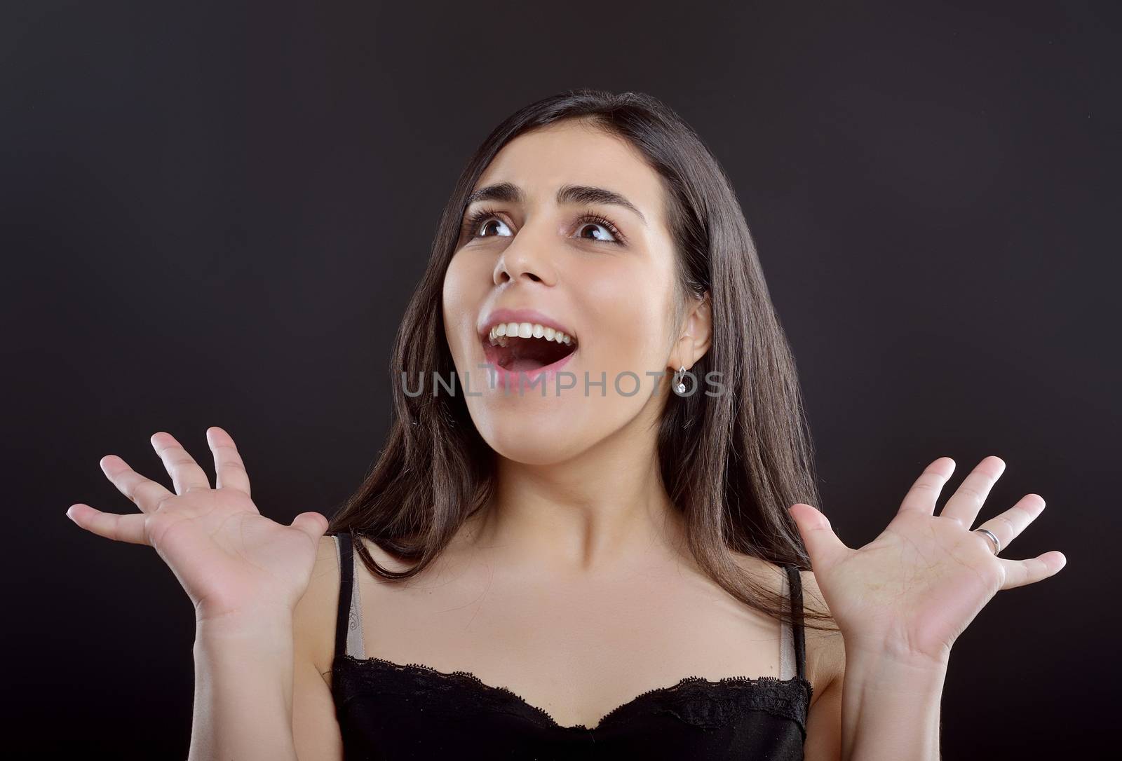 Beauty portrait of a young girl who surprisingly shrugs to the side and stands on a black background