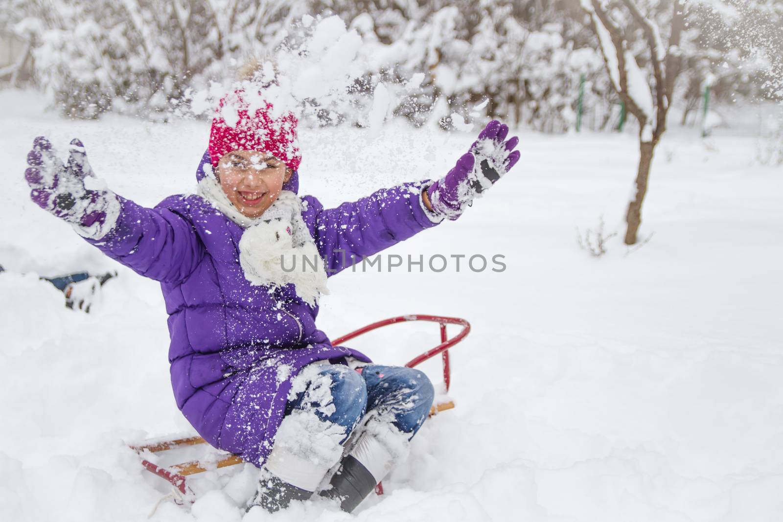 Happy child girl in park on sledge playing with snow