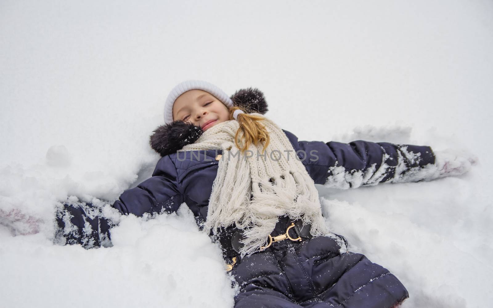 Happy child girl lying on snow in winter park