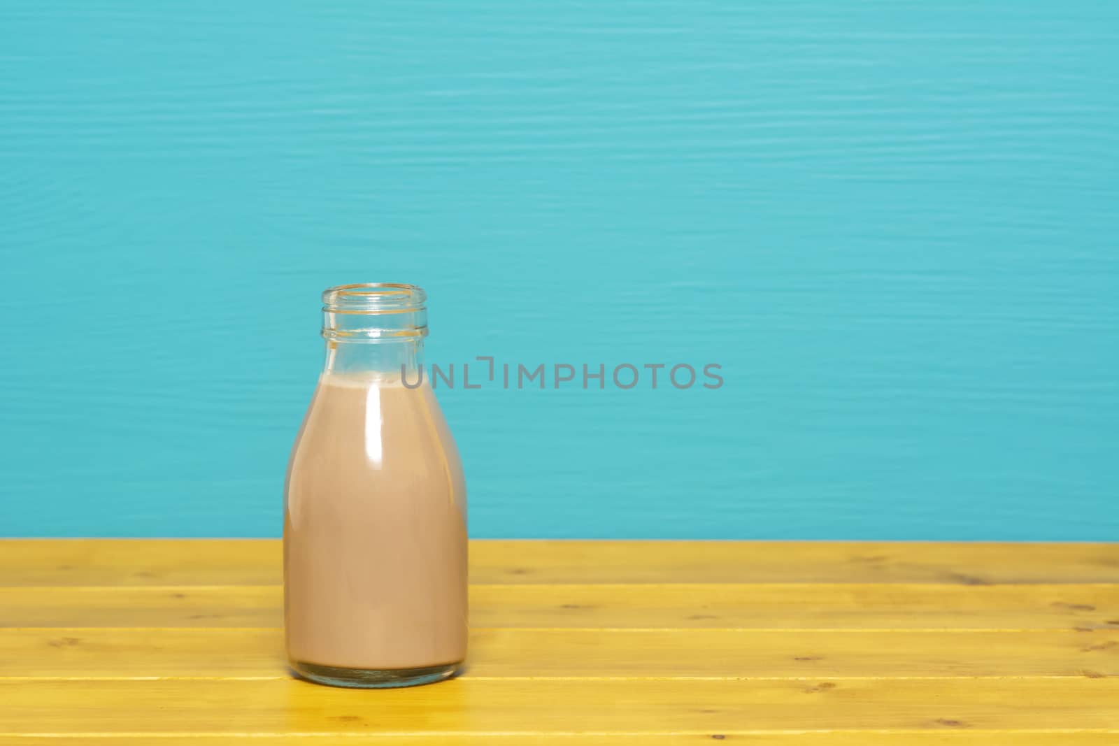 Chocolate milkshake in a one-third pint glass milk bottle, on a wooden table against a bright teal painted background