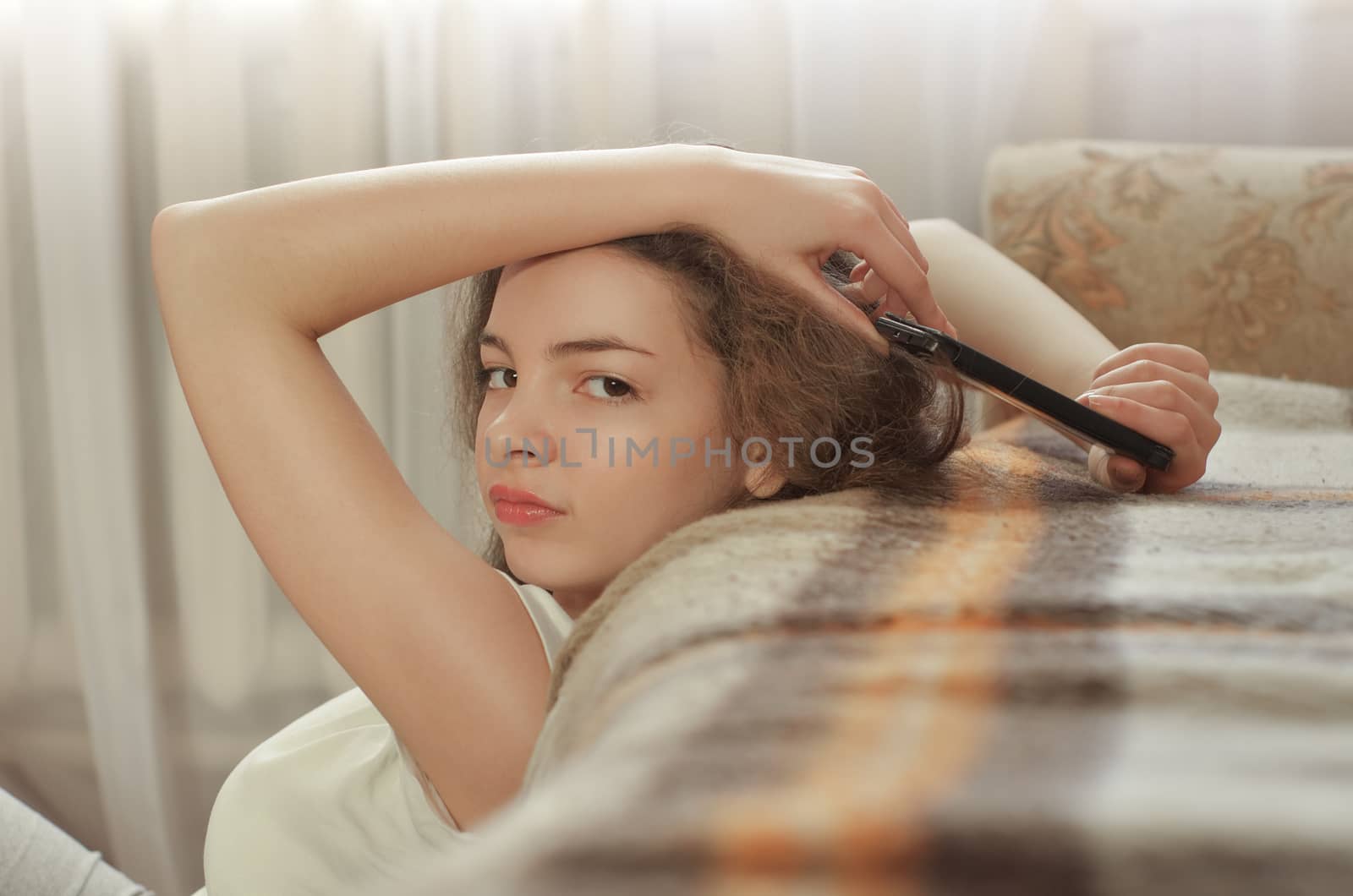 Cheerful brunette girl talking on mobile phone while sitting on comfortable couch. Smiling hipster girl having cell telephone conversation while resting near sofa