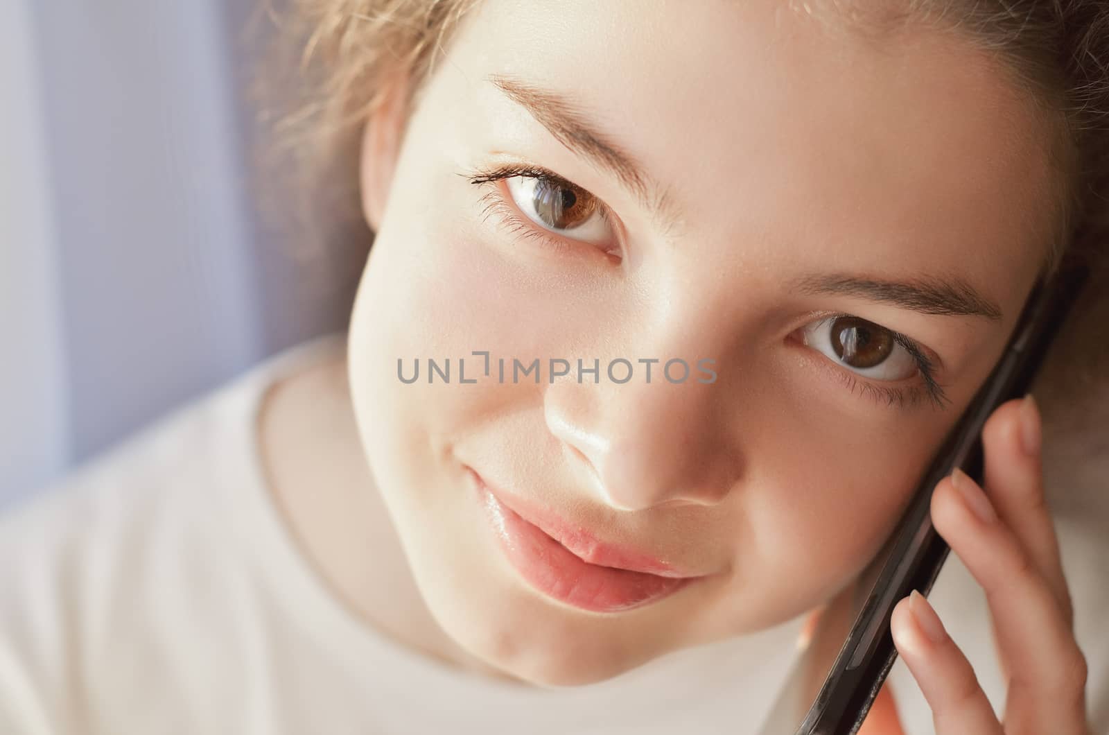 Portrait of a beautiful girl who speaks by telephone at home near windows, clouse-up