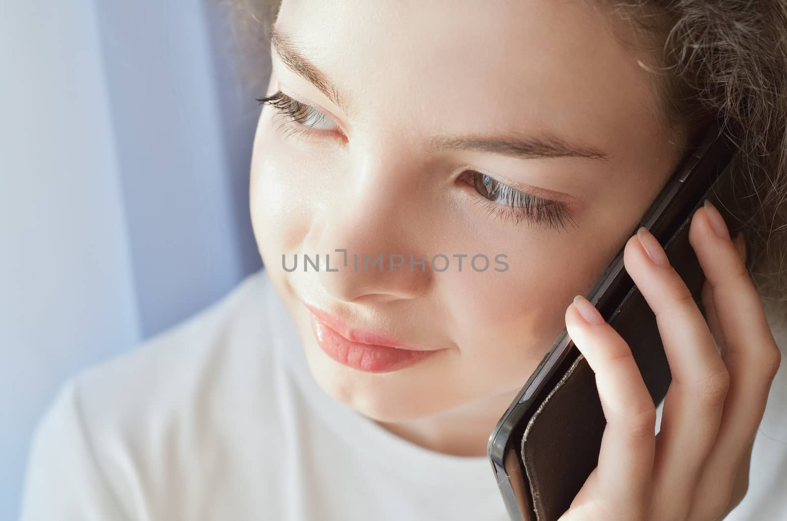 Portrait of a beautiful girl who speaks by telephone at home near windows, clouse-up