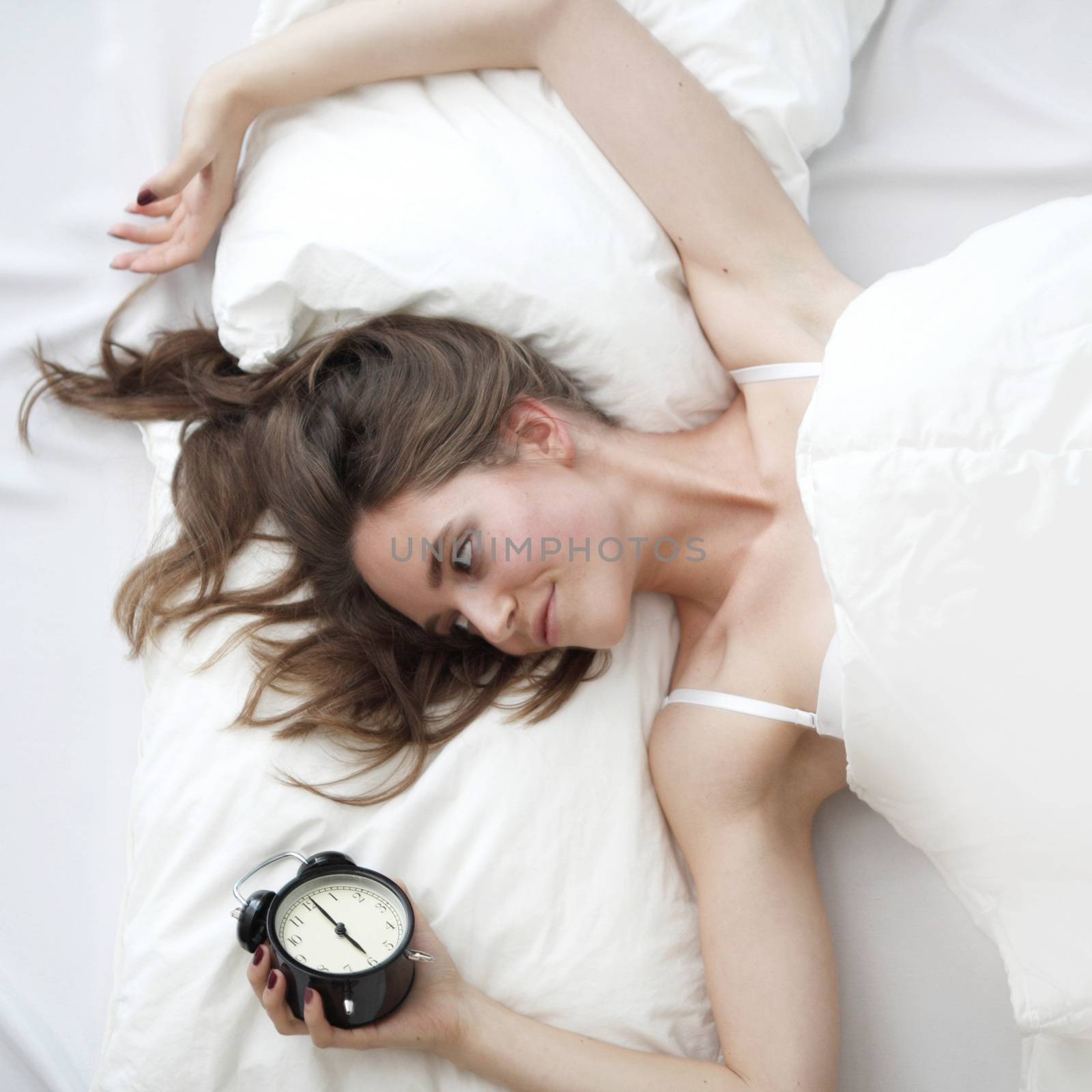 Young beautiful woman waking up with alarm clock