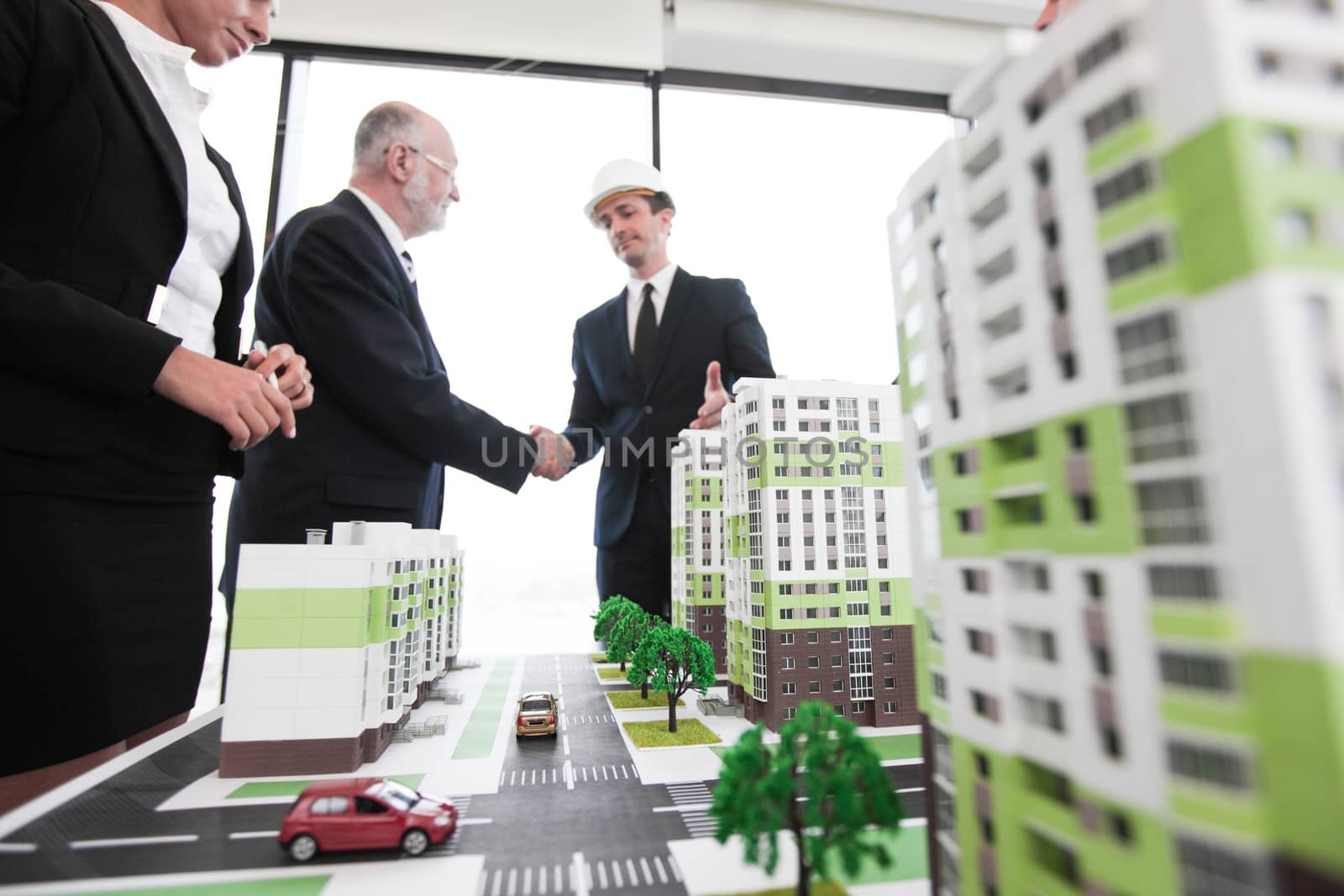 Business handshake of architect and investor looking at model of residential quarter houses