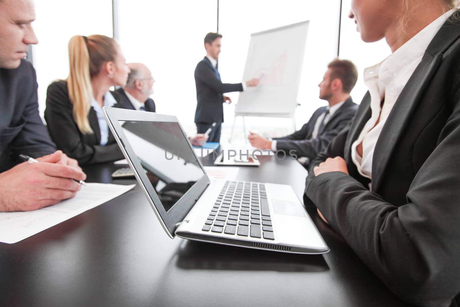 Mixed group of people in business meeting working with documents and computers man with presentation at flipchart