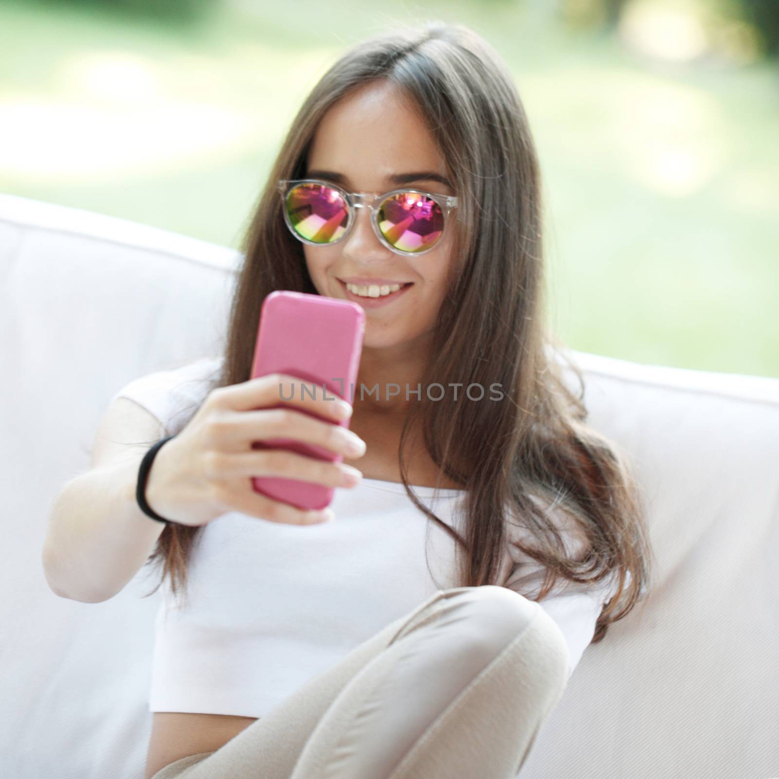 Beautiful young girl with smartphone sitting outdoors making selfie