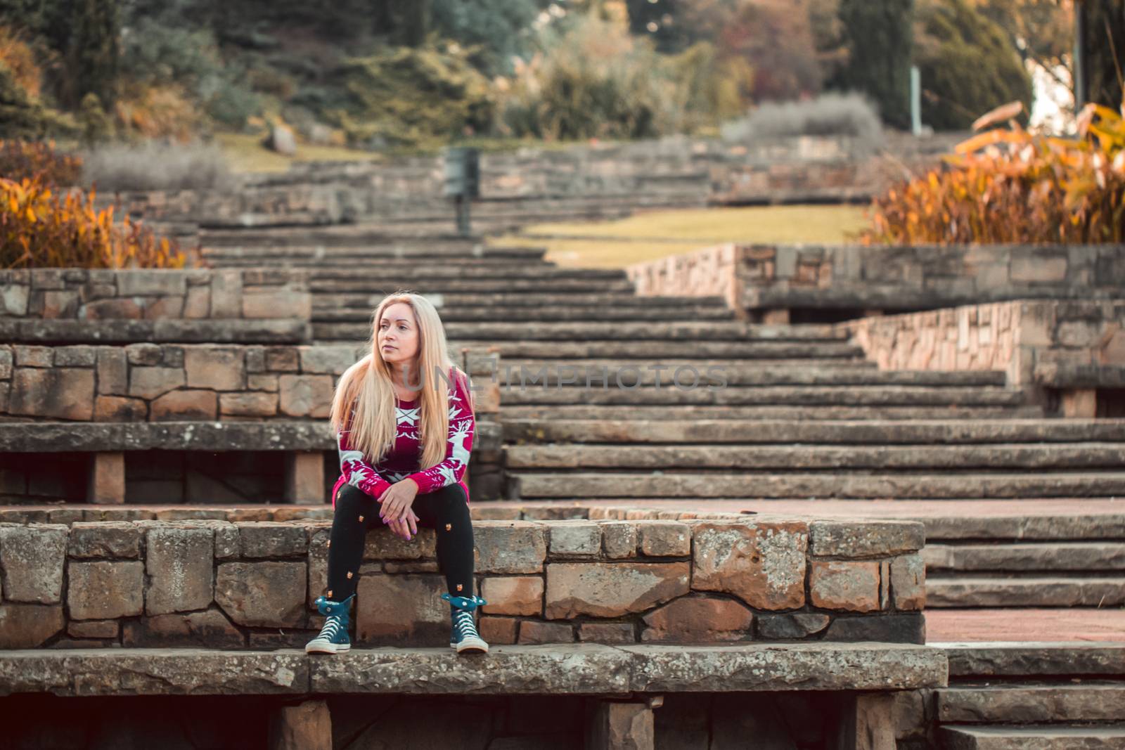 Woman sitting on stone steps in an autumn or fall forest park. by Anelik