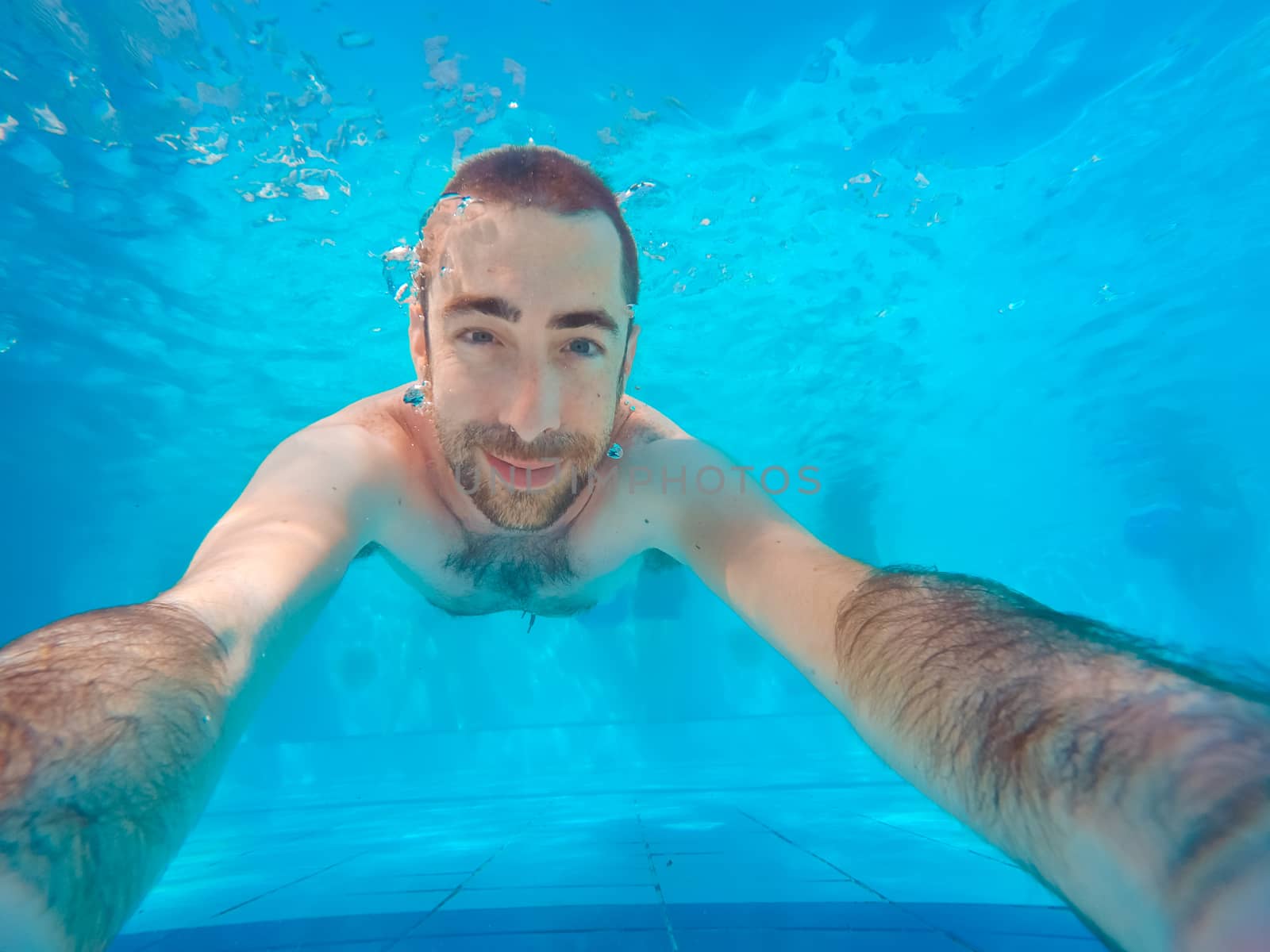 Young handsome man diving underwater in a swimming pool. He smiling and looking at camera.