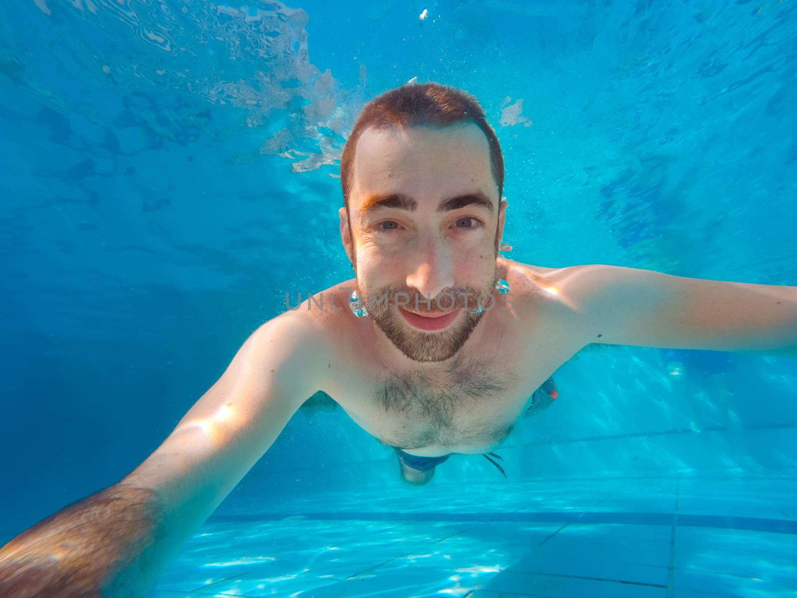 Young handsome man diving underwater in a swimming pool. He smiling and looking at camera.