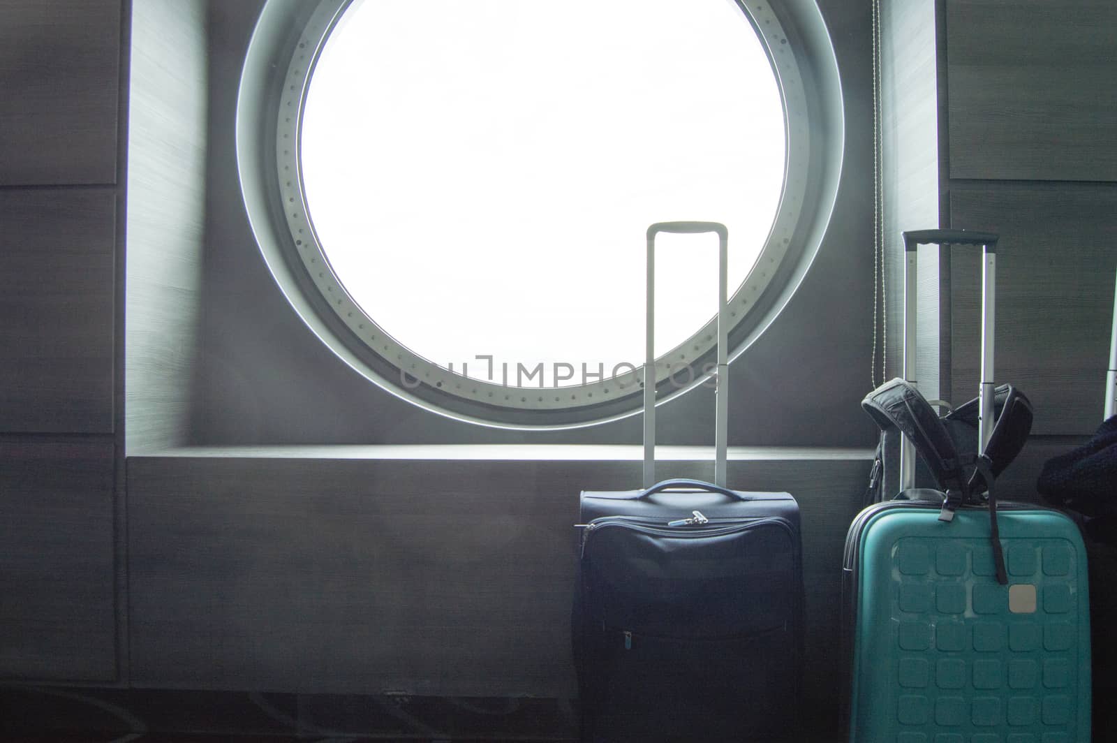 Two suitcases for traveling in front of the round porthole of the ship, the concept of leisure or business trip.