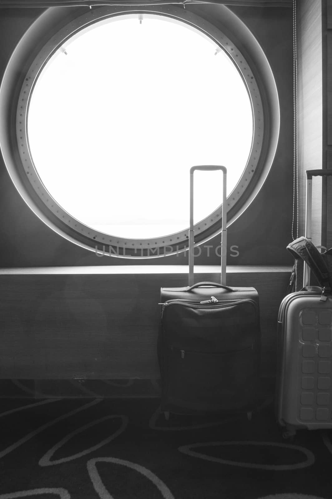 Two suitcases for traveling in front of the round porthole of the ship, the concept of leisure or business trip, vertical shot.