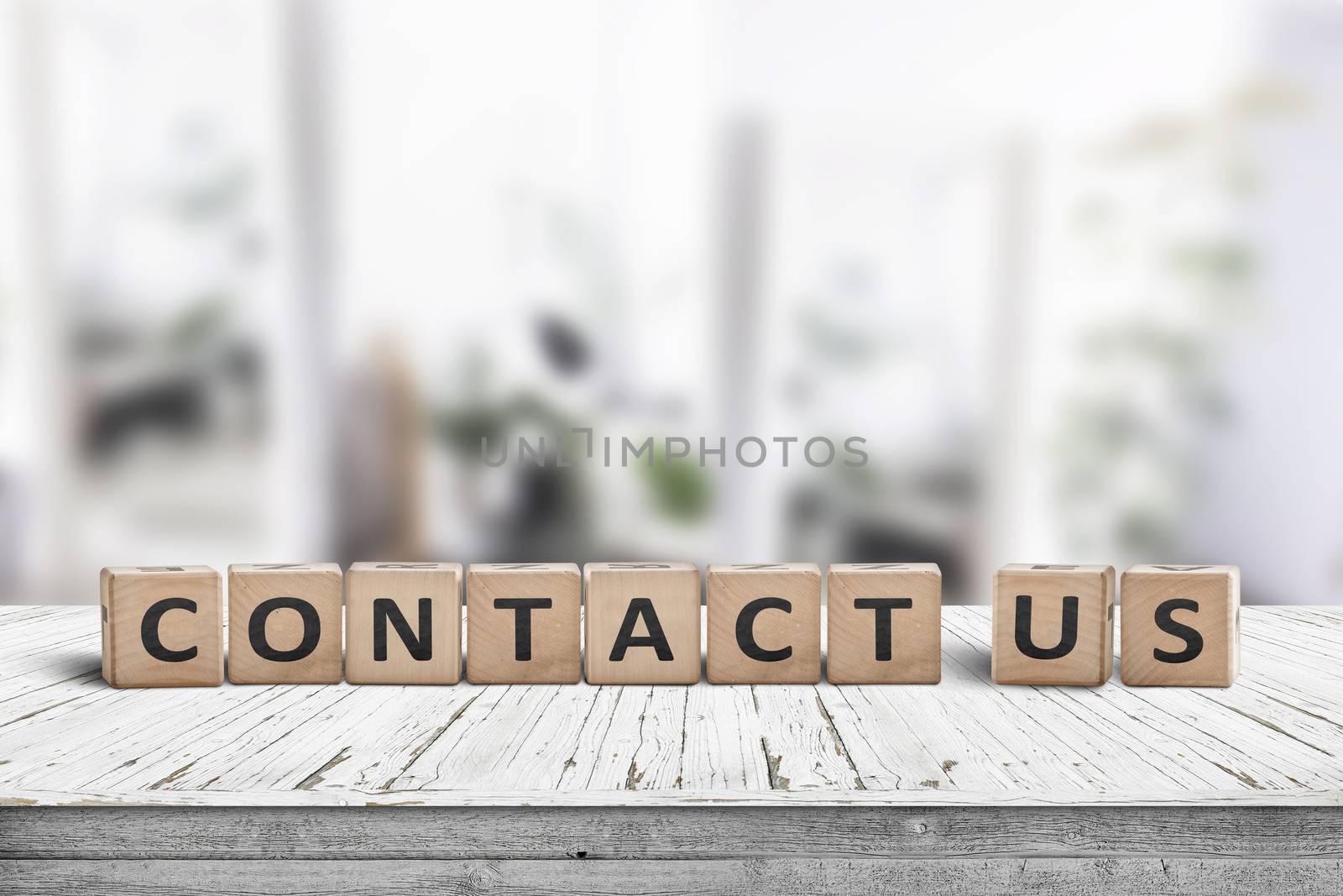 Contact us sign on a wooden desk in a bright living room with green plants