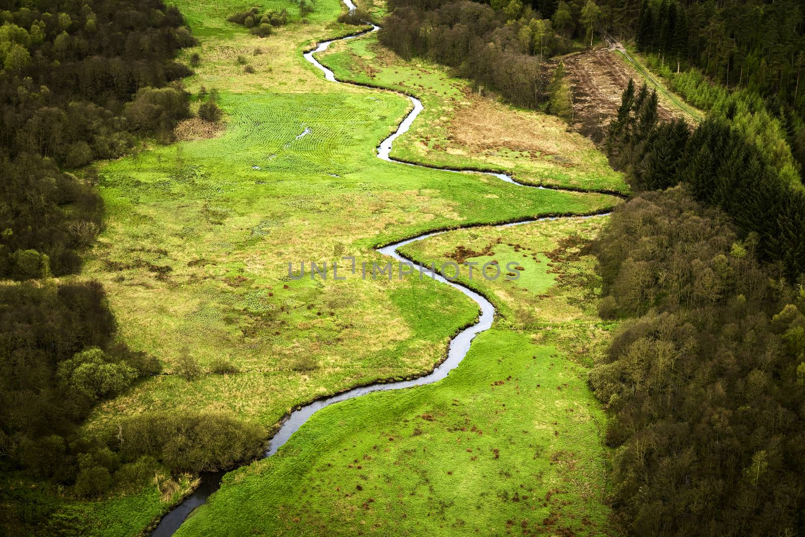 Small river going through a green area with fields and trees seen from above