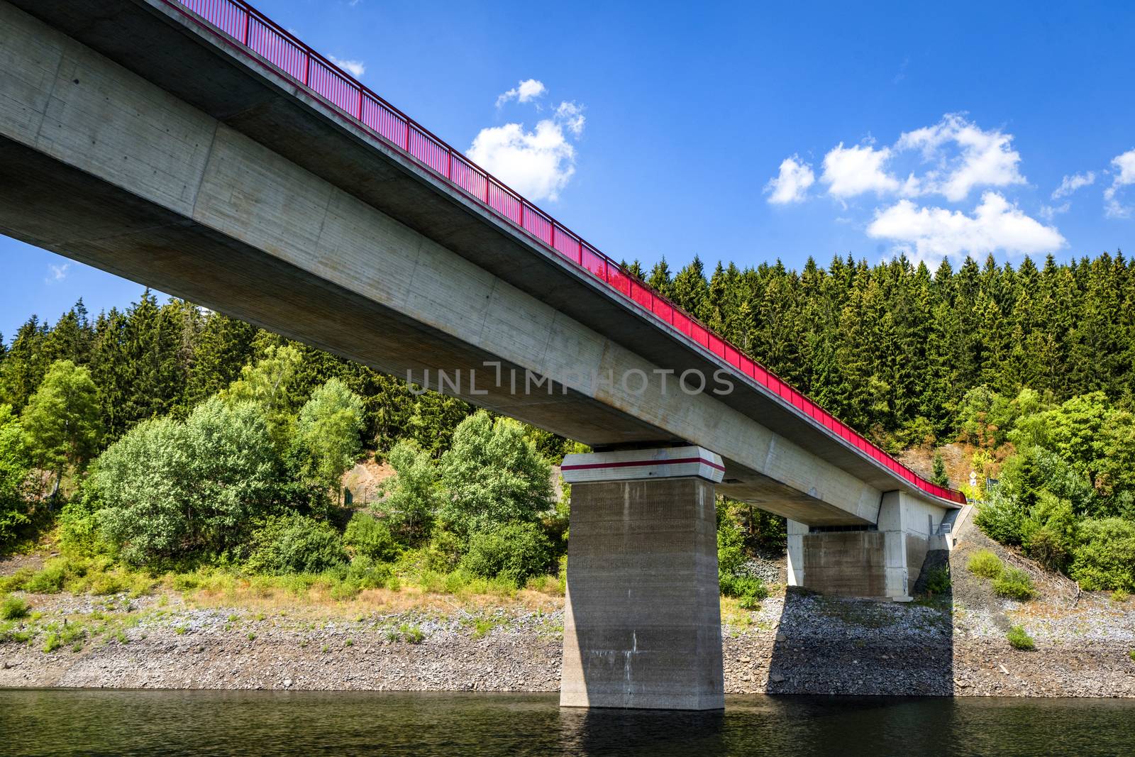 Bridge with red fence over a lake in the summer with a forest in the background