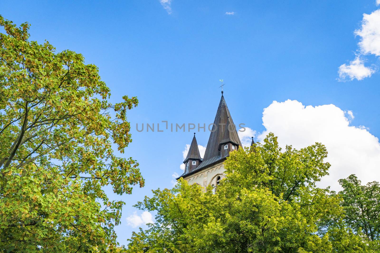 Fairytale castle tower rising up behind green trees in the spring with blue sky above