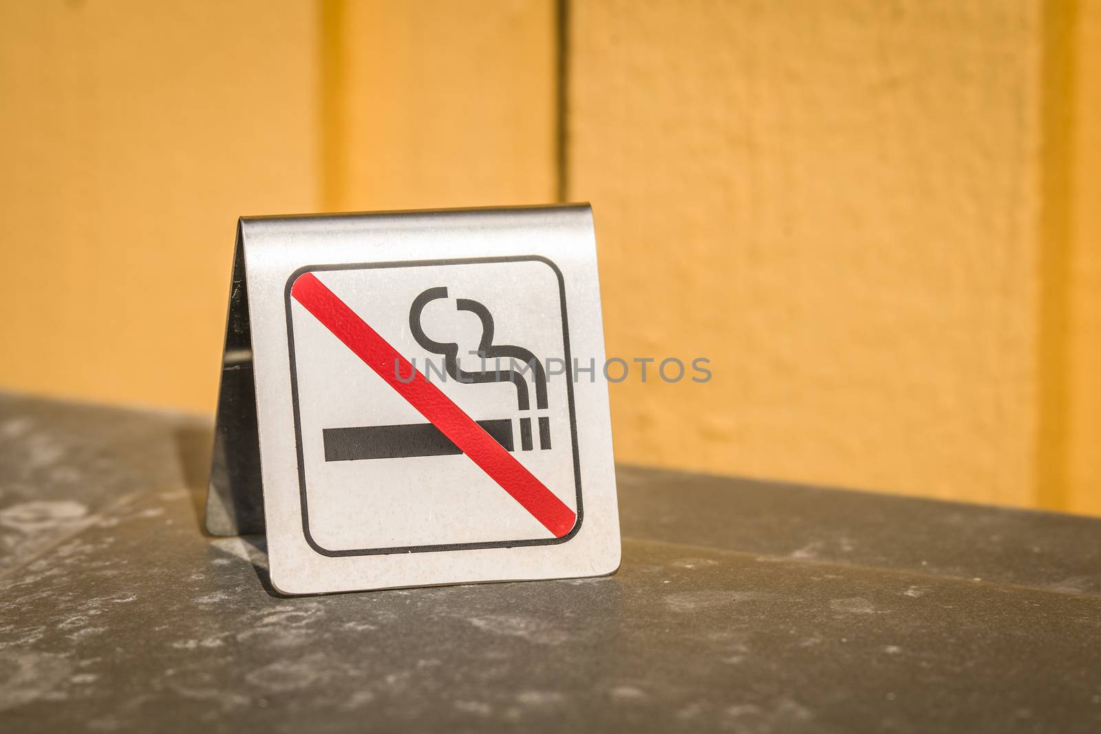 No smoking metal sign on a table with a yellow wall in the background