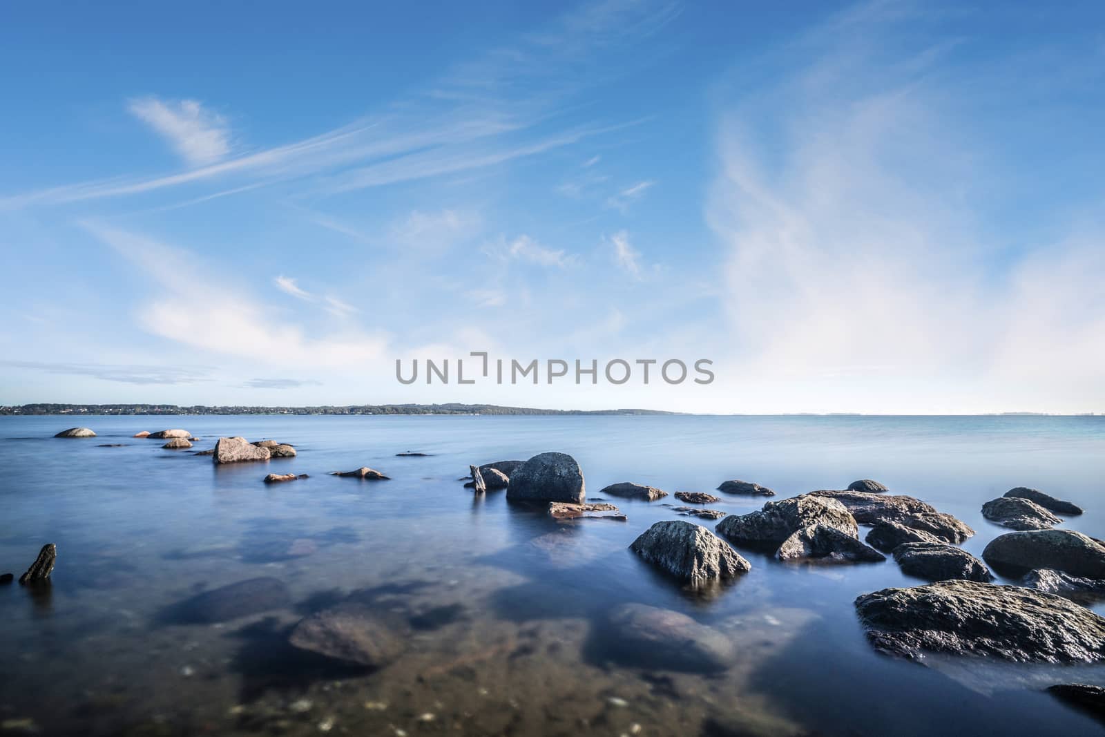 Rocks by the ocean in the calm water under a beautiful blue sky