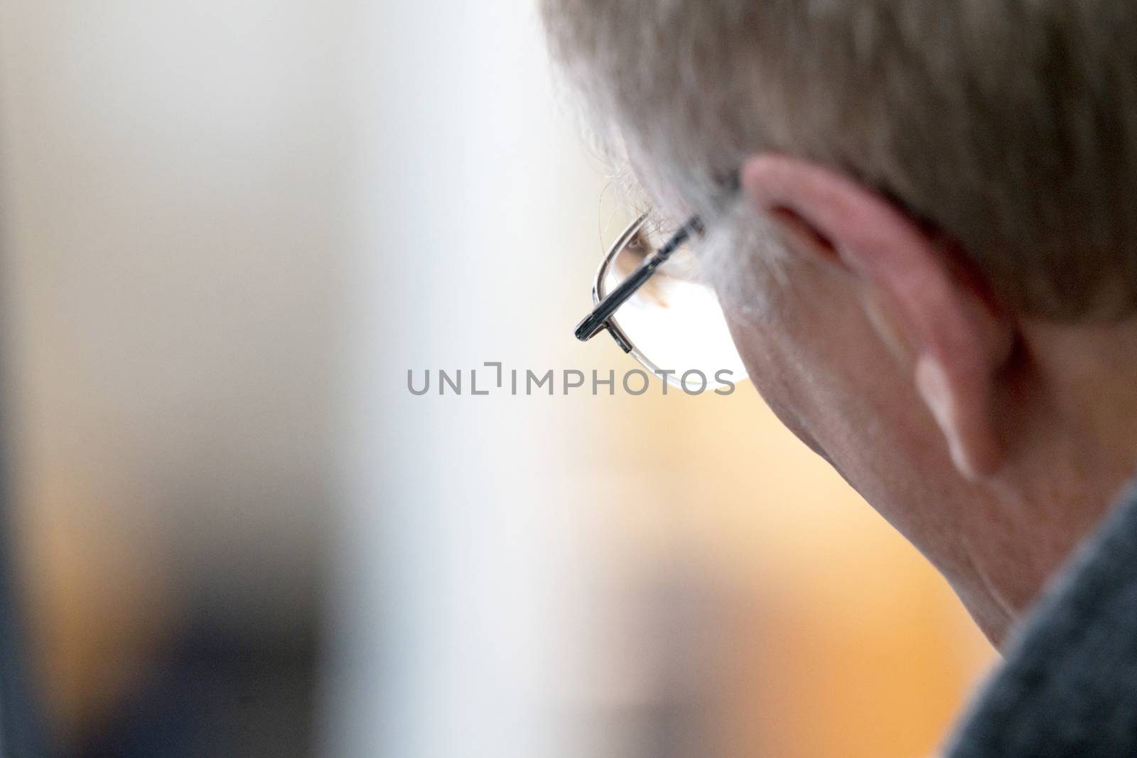 Senior male looking through a pair of glasses at an office with golden colors in the background