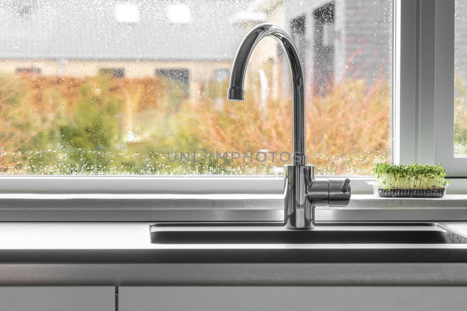Chrome faucet by a kitchen sink with a wet window in the background
