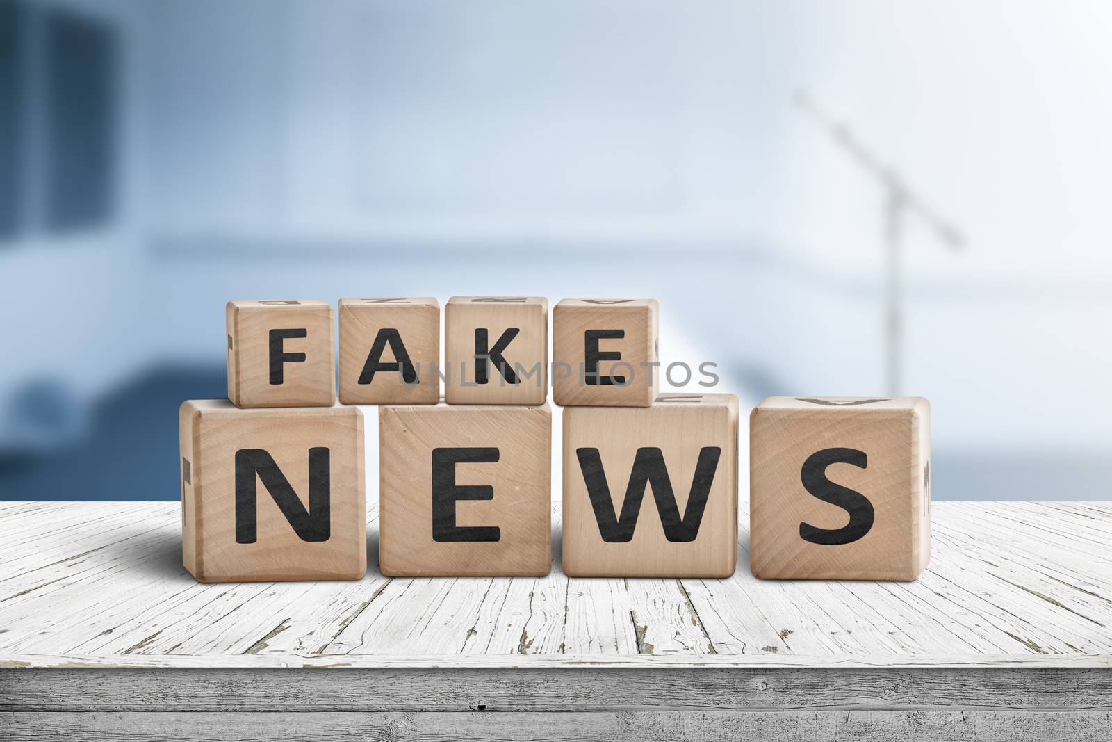 Fake news sign on a wooden desk in a blue room with a blurry background