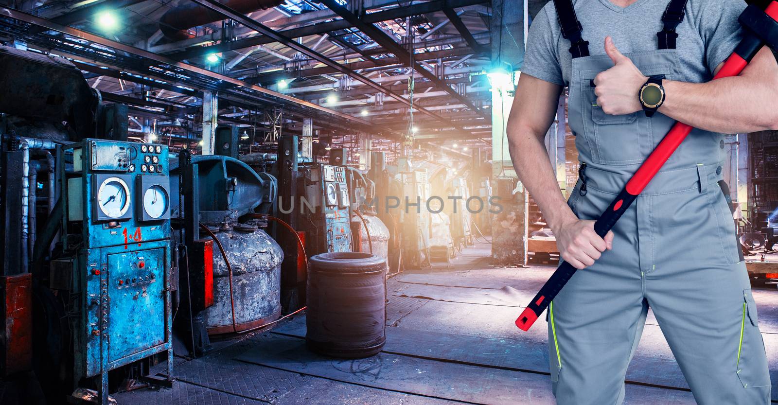 Closeup of worker man with ax dressed in overalls on Industrial zone background, manufacturing facility. Concept of Safe labor in the enterprise.