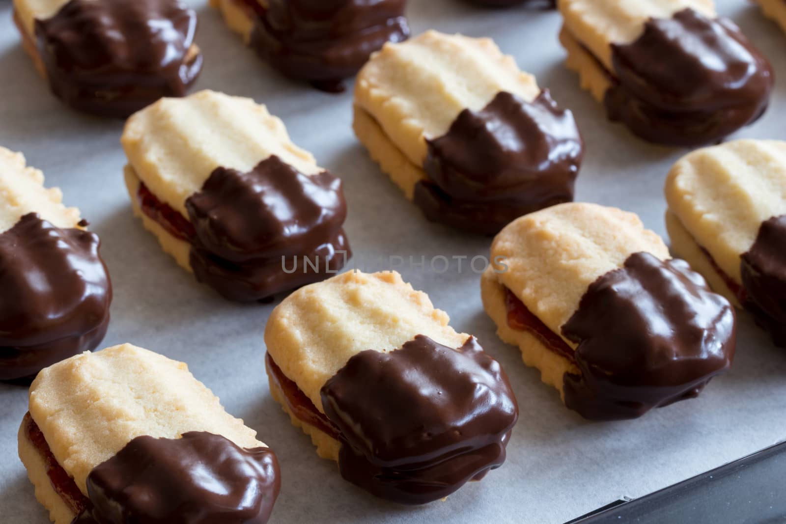Christmas cookies filled with jam and dipped in chocolate on a baking sheet