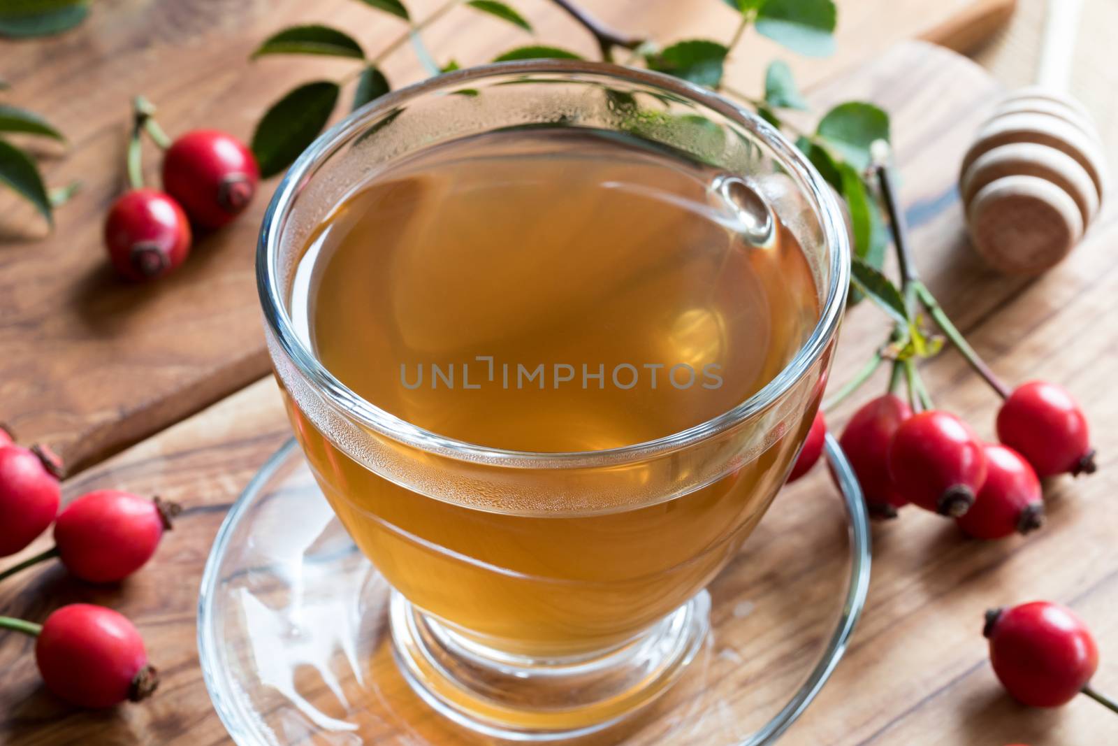 A cup of rosehip tea on a wooden table, with fresh rosehips in the background