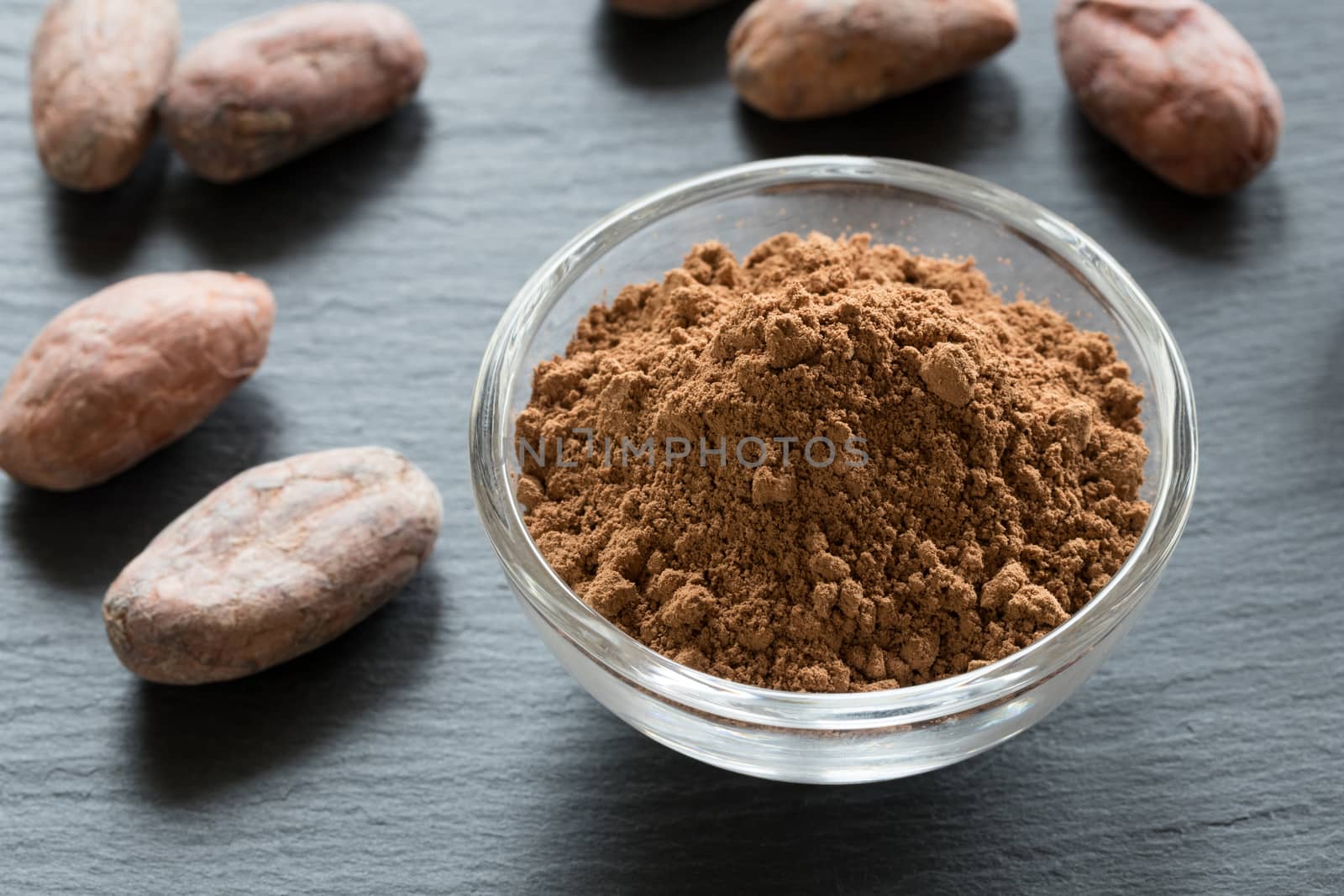 Raw cocoa powder, with raw cacao nibs in the background