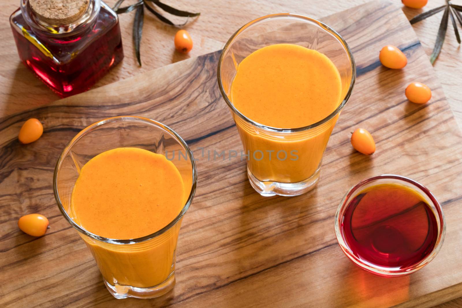 Two glasses of sea buckthorn juice, with sea buckthorn oil and berries in the background