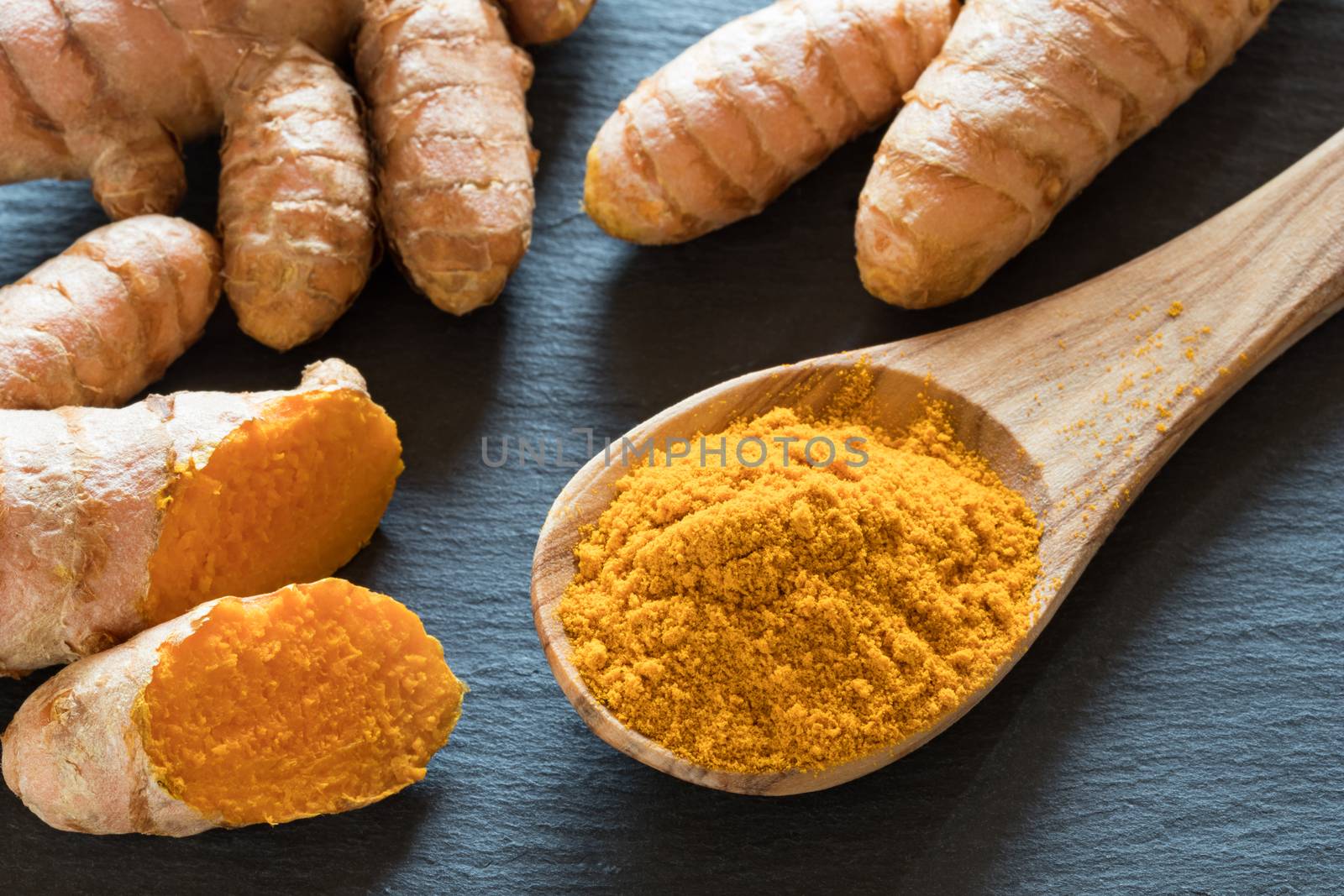 Turmeric powder on a wooden spoon, with fresh turmeric root in the background