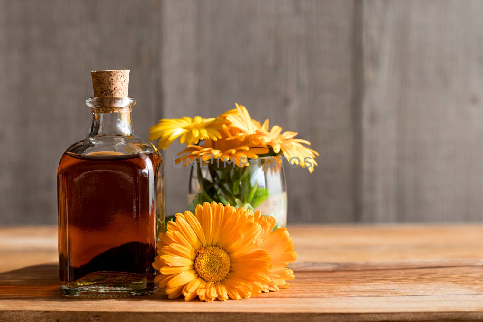 A bottle of calendula (marigold) tincture with fresh calendula flowers on a wooden background