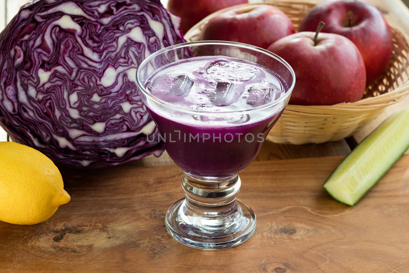 Purple cabbage juice in a glass, with cabbage, apples, cucumber and lemon in the background