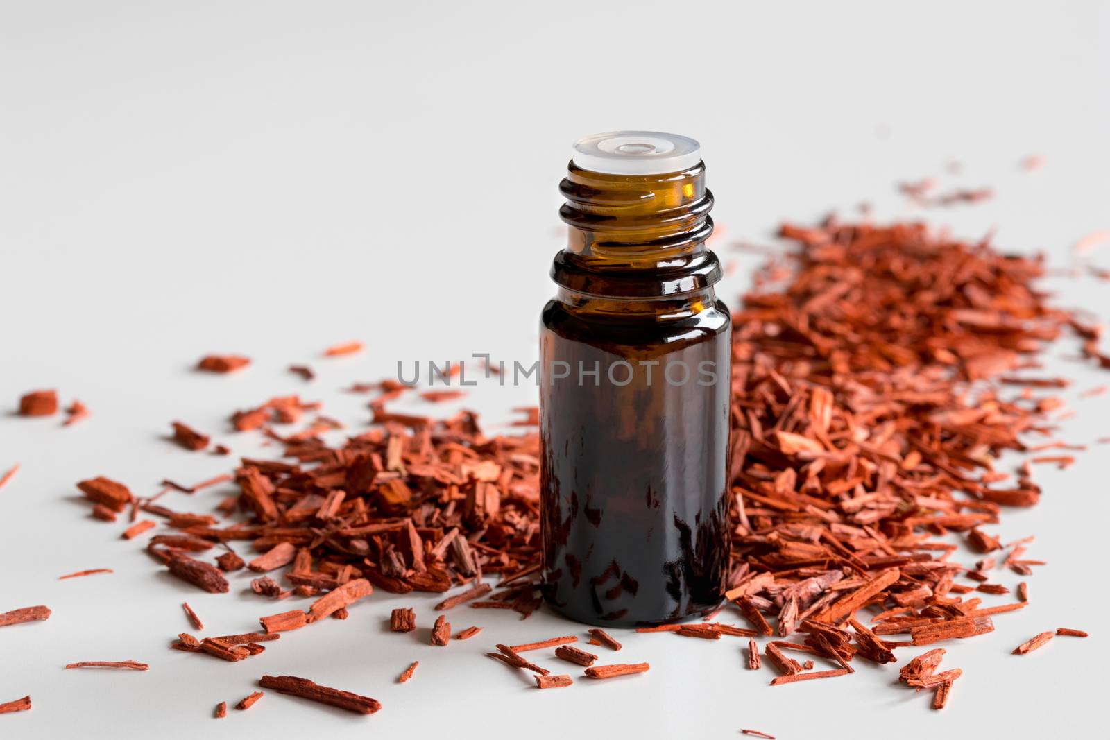 A bottle of sandalwood essential oil with sandalwood on a white background