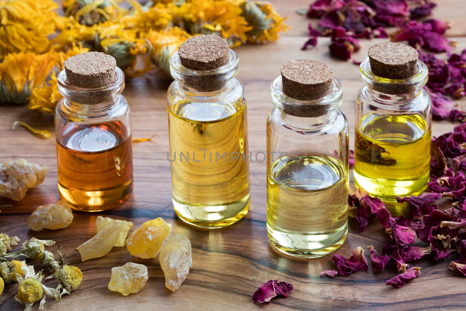 Bottles of essential oil with dried rose petals, chamomile, calendula and frankincense on a wooden table