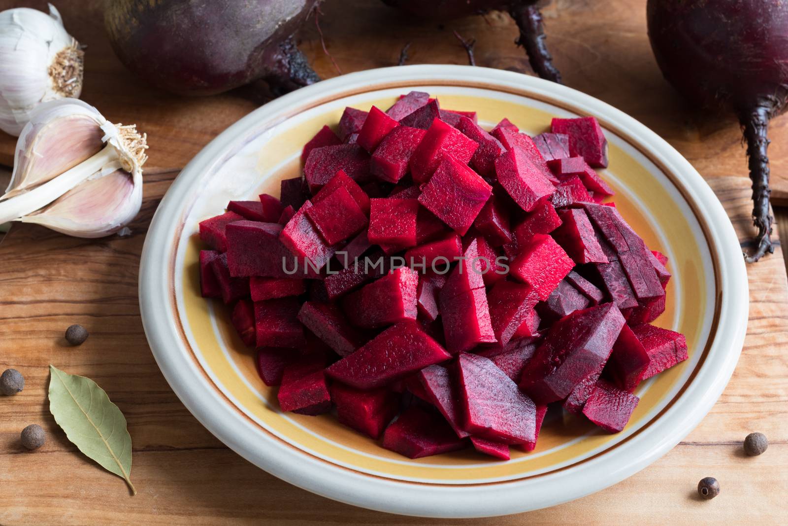 Preparation of fermented beets - sliced red beets on a plate, with whole beets, onions, garlic and spices in the background