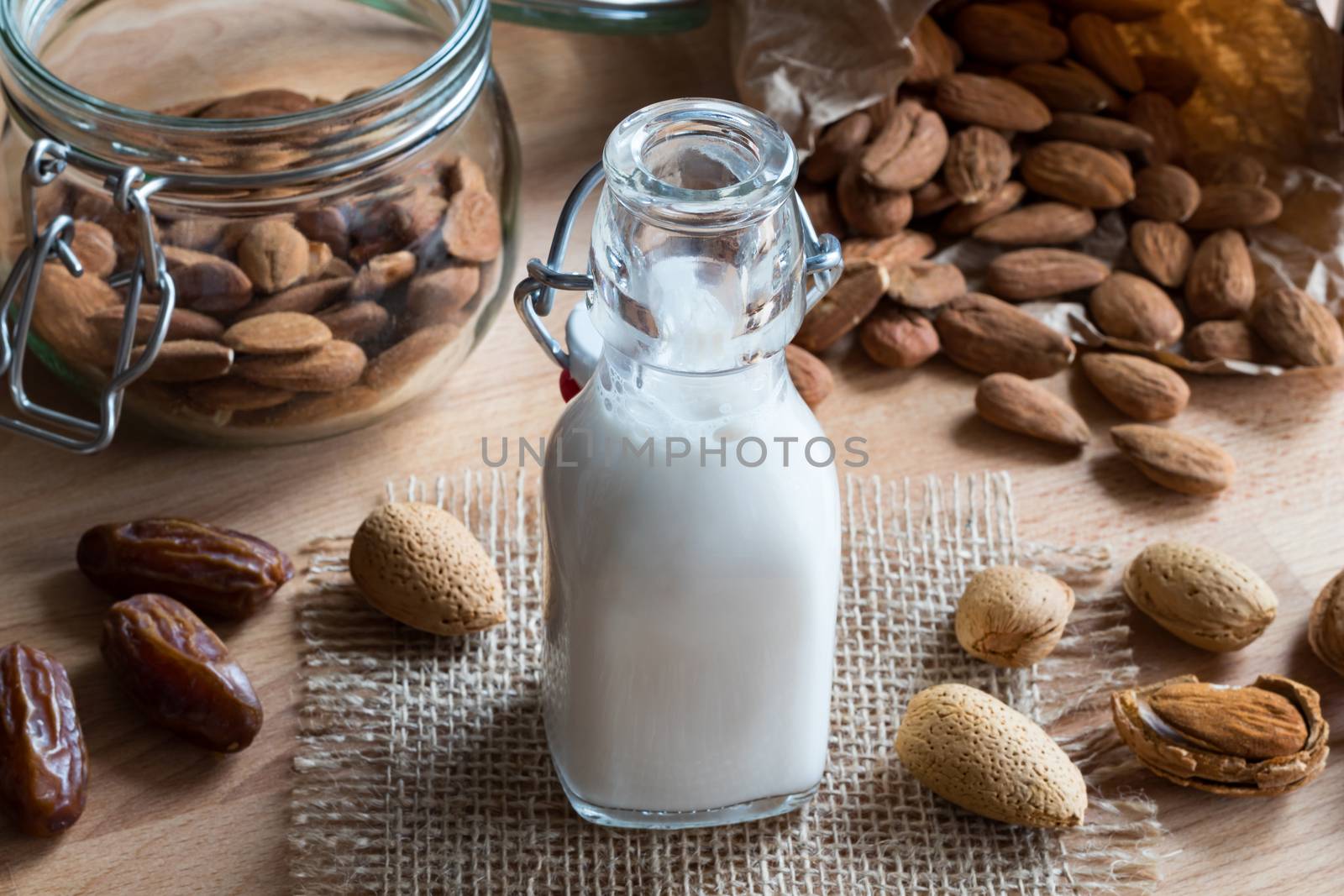 A bottle of almond milk on a wooden table with almonds and dates