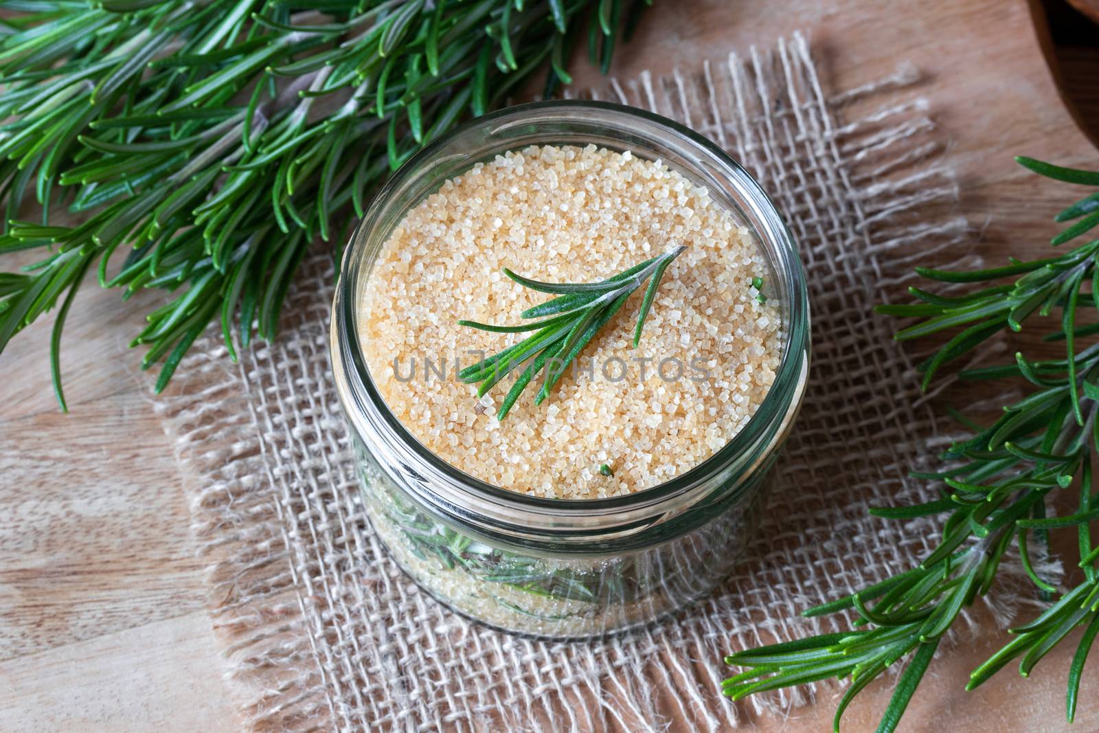 A jar filled with fresh rosemary and cane sugar, to prepare homemade herbal syrup