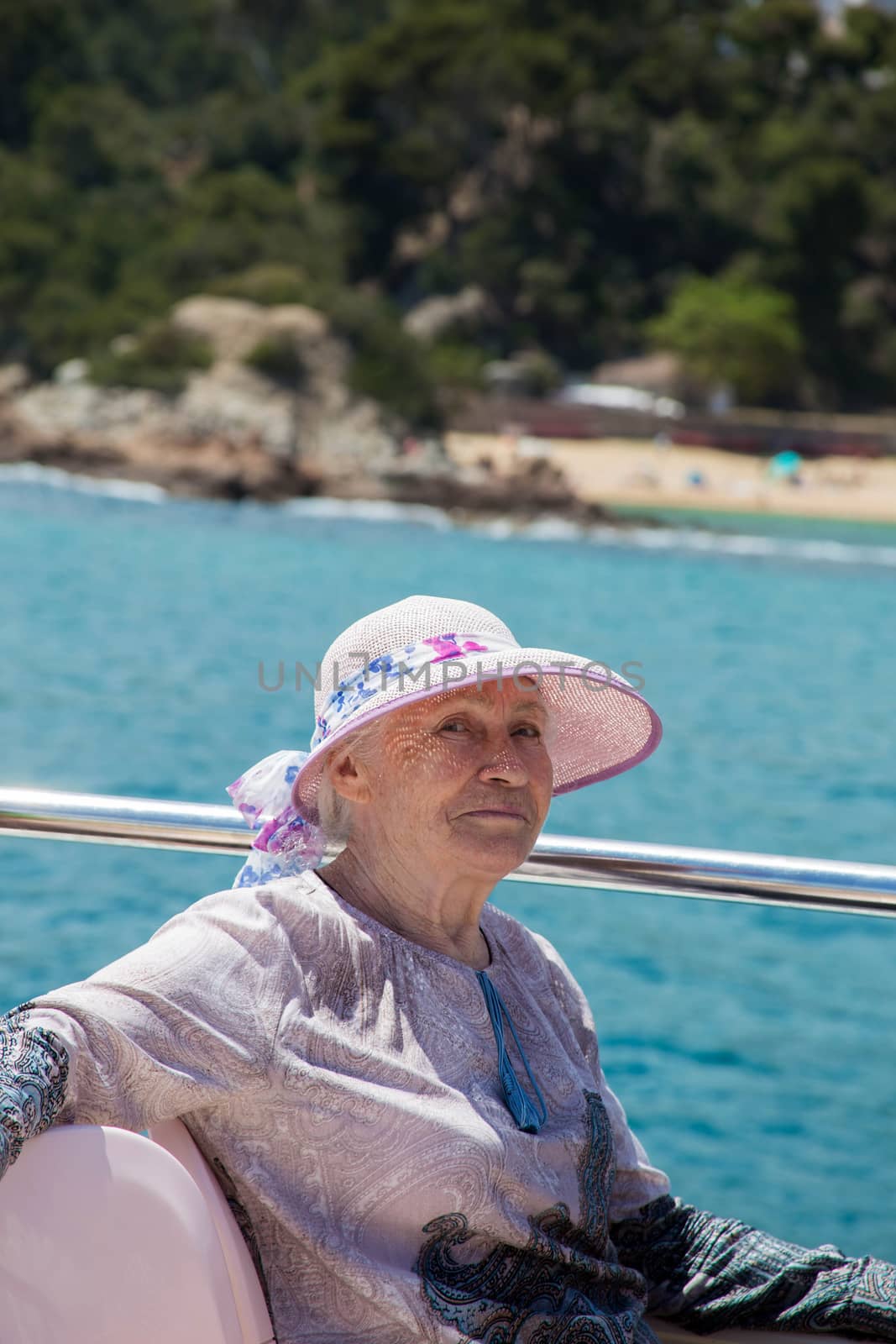 Elderly pretty woman in sun-hat enjoys summer vacation in a sea voyage on a pleasure boat. She sits on the upper deck